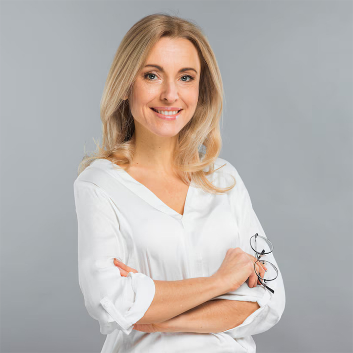 Kathy is a confident middle-aged woman in a white blouse holding glasses, smiling against a gray background