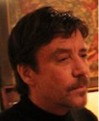 Portrait of Dr. Scott, PhD, LMFT with dark hair and a mustache, wearing a dark shirt in a warmly lit room.