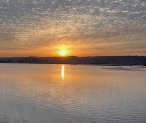 A golden sunset casts its reflection over a calm body of water, with rippling waves and a softly clouded sky in Egypt.
