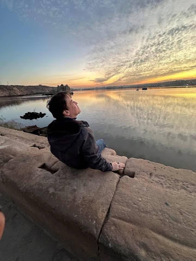 Dr. Scott, PhD, LMFT sitting on a stone ledge overlooking a calm river at sunset, gazing peacefully at the sky in Egypt.