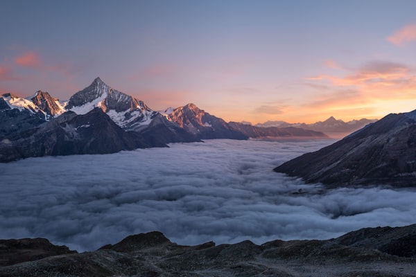 Snow-covered mountain peaks above a sea of clouds at sunrise with a colorful sky.